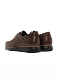 Chaussures en cuir marron avec une forme arrondie, présentant une texture lisse, un petit talon et une semelle en caoutchouc noire. Détail de lacets à l'avant.