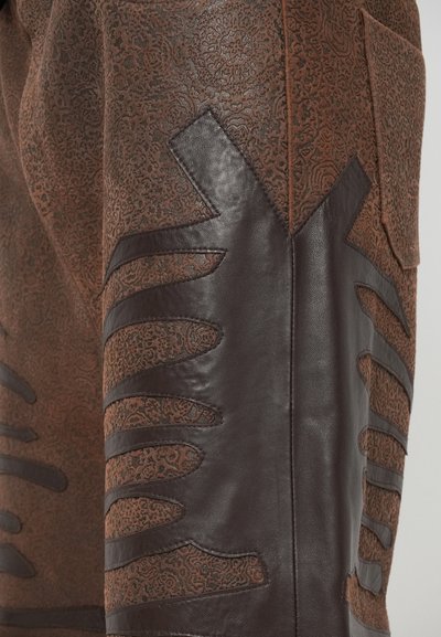 Bruine leren broek met een geperst bloemenpatroon, met donkerbruine uitsnijdingen aan de zijkanten, wat zorgt voor een gestructureerd ontwerp.