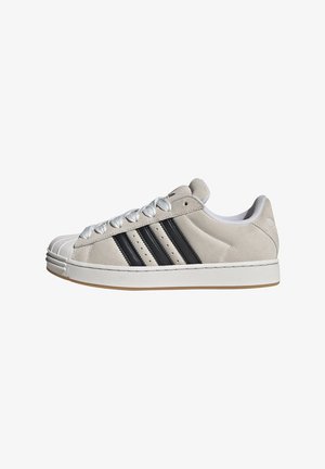 Svetlo sivi semiš športni copat z belo gumijasto podplatom, tremi črnimi črtami in teksturirano kapico na prstih. Ima bele vezalke in oblazinjen ovratnik.