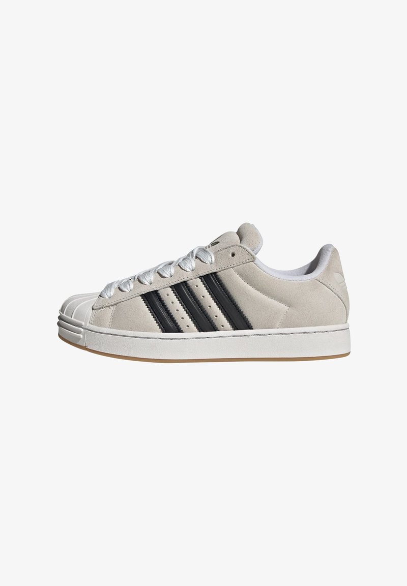 Svetlosivá semišová teniska s bielou gumovou podrážkou, tromi čiernymi pásikmi a textúrovanou špičkou. Má biele šnúrky a vystlaný golier.