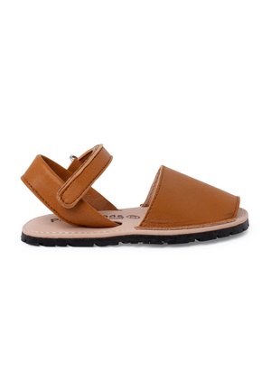 Sandaña de cuero marrón con puntera cerrada, talón abierto y correa ajustable de velcro. Presenta una suela de goma texturizada y un forro interior suave.