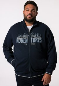 Navy zip-up jacket with mountain graphic and "ADVENTURES" text. Features ribbed cuffs and hem with light gray stripes. Smooth fabric texture.