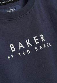 Tummansininen puuvillapaita, jossa on näyttävää valkoista tekstiä: "BAKER BY TED BAKER" modernilla fontilla. Paidassa on resoritettu pyöreä kaula-aukko ja sileä pinta.