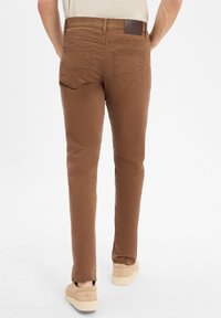 Pantalons slim en coton marron, avec une texture lisse, cinq poches et une discrète étiquette logo sur la ceinture arrière.
