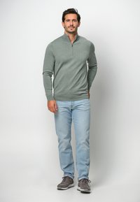 Herren leichter grauer Reißverschluss-Pullover, taillierte Passform, gerippte Bündchen und Saum, kombiniert mit hellblauen Jeans und grauen Sneakers.