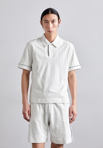 Hvid polo-shirt og shorts sæt med et fiskebensmønster, der har krave, korte ærmer og kontrasttrim på ærmerne og shortsene.