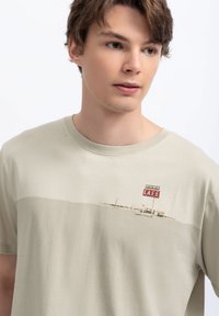 Beige katoenen t-shirt met een grafisch ontwerp van een cafébord met rode letters. Ronde hals, korte mouwen, zachte textuur, casual pasvorm.