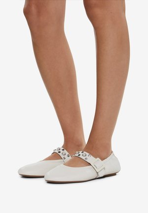 White leather ballet flats with ankle strap, adorned with silver studs and a buckle, featuring a rounded toe and flat sole.