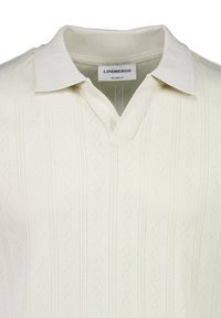 Polo en maille couleur crème avec des motifs subtils en zigzag et des rayures verticales, avec une coupe décontractée et un col.