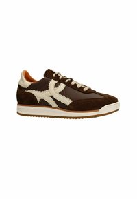 Brown suede sneakers with cream accents, featuring a textured design, lace-up closure, and rubber sole. Notable stitching detail along sides.