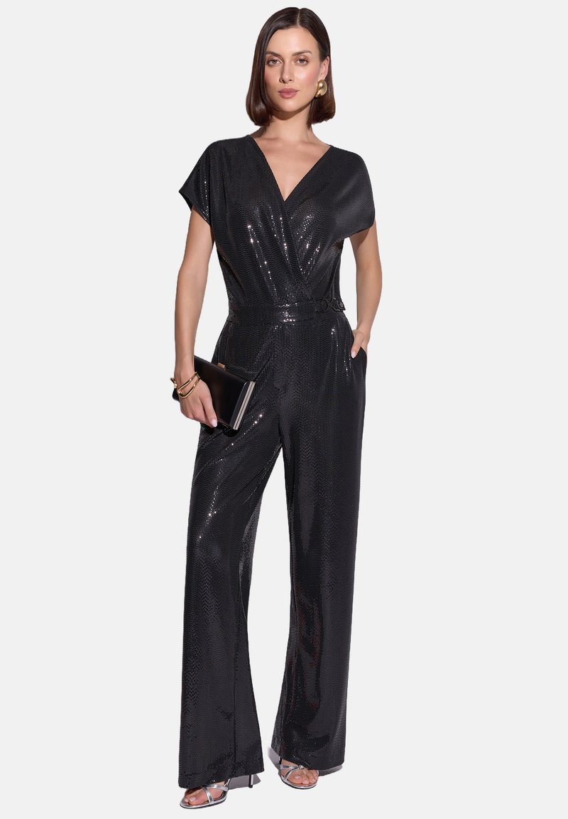 Czarny kombinezon z krótkimi rękawami, dekoltem w kształcie litery V i paskiem w talii. Wykonany z błyszczącego, teksturowanego materiału, z szerokimi nogawkami; zestawiony z metalicznymi szpilkami.