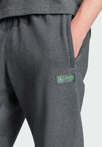 Mörkgrå sweatpants i blandad bomullstyg. Har sidfickor, en grön logotypmärke med ett varumärkesemblem och elastisk midja.