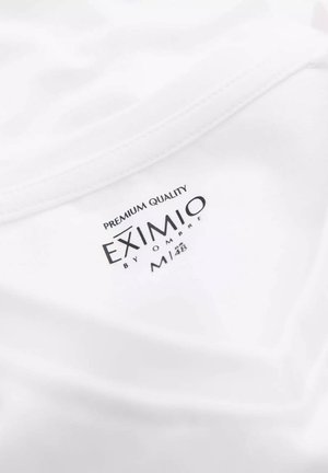 Camiseta blanca de tela suave; presenta una etiqueta impresa que dice "CALIDAD PREMIUM EXIMIO by OMBRE M 48" en negro.
