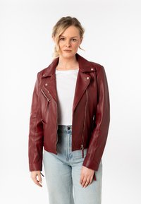 Bordeaux leren motorjack met asymmetrische rits, metalen hardware en twee ritszakken, gecombineerd met een witte top en lichte jeans.