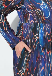 Abito multicolore con un motivo ondulato in tessuto blu, arancione e nero, con maniche lunghe e tasche laterali.