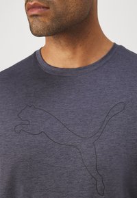 Mørkeblå t-skjorte laget av teksturert stoff, med en svart PUMA-logo i en hoppende posisjon over brystet og rund hals.