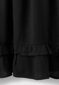 Tissu noir avec une surface texturée présentant un détail de volants horizontaux près de l'ourlet, sur un fond blanc.