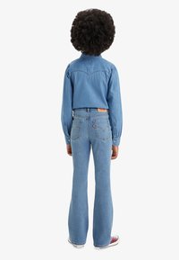 Denimhemd mit langen Ärmeln in einem verblassten hellblauen Farbton, kombiniert mit hellblauen, ausgestellten Jeans mit einem Levi's-Logo auf der Rückseite.
