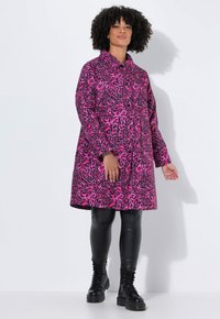 Rosa Leopardenmuster-Mantel mit Kragen, langen Ärmeln und lockerer Passform. Tragen über schwarzen Leggings und abgerundet mit schwarzen Schnürstiefeln.