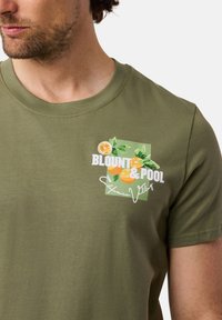Oliven grøn t-shirt i bomuld med et grafisk design af appelsiner og blade samt teksten "BLOUNT & POOL" i fed hvid skrift.