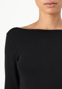 Top lungo a maniche nere a costine con scollatura a barca ampia. Texture liscia con design aderente, che enfatizza l'area del seno e delle spalle.