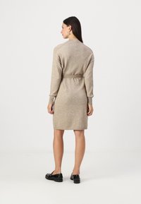 Abito lavorato a maglia beige con maniche lunghe, vita aderente e dettaglio con cintura. Polsini e orlo a coste, texture liscia, design di lunghezza media.