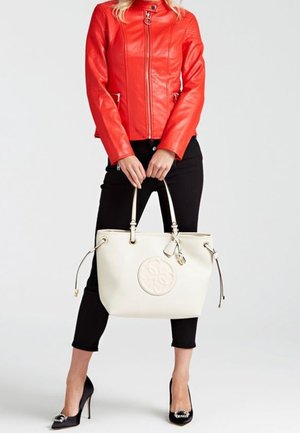 Bolso tote de cuero blanco con un logotipo circular y lados con cordón, combinado con una chaqueta de cuero roja, pantalones negros y tacones altos negros.