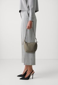 Geantă puffer de culoare verde măsliniu cu un mânere scurt, purtată cu o ținută alb-negru în carouri houndstooth și cu tocuri stiletto negre.