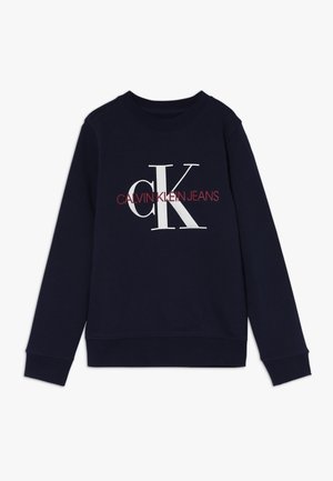 Sweatshirt en coton bleu marine à manches longues, avec des poignets et un col côtelés. Il présente un logo "CK" blanc et le texte "CALVIN KLEIN JEANS" en rouge.
