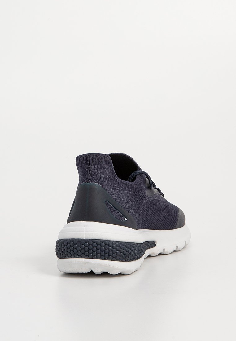Botte de sport tricotée marine avec une semelle blanche texturée, dotée d'un tirant à l'arrière et de détails en accent foncé lisse. Design à lacets avec rembourrage.