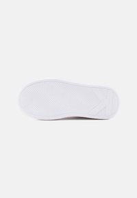 Λευκή σόλα αθλητικού παπουτσιού με υφασμένο κυματιστό σχέδιο πρόσφυσης και ανάγλυφο γράμμα "K" κοντά στη φτέρνα, σε απλό λευκό φόντο.