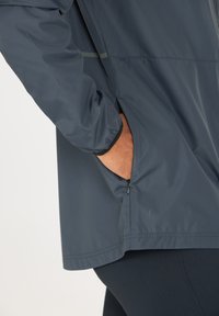 Vattentålig marinblå jacka med en zippered ficka, elastiska muddar och en jämn textur. Plagget har en avslappnad passform och minimal detaljering.