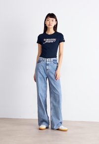 Námořnické tričko s logem "Tommy Jeans", spárované se světle modrými, širokými džíny a bílými teniskami se žlutými podrážkami.