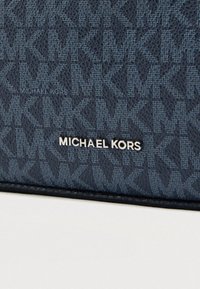 Granatowy portfel Michael Kors z monogramem, teksturowaną powierzchnią i srebrnym logo w eleganckiej czcionce na przodzie.