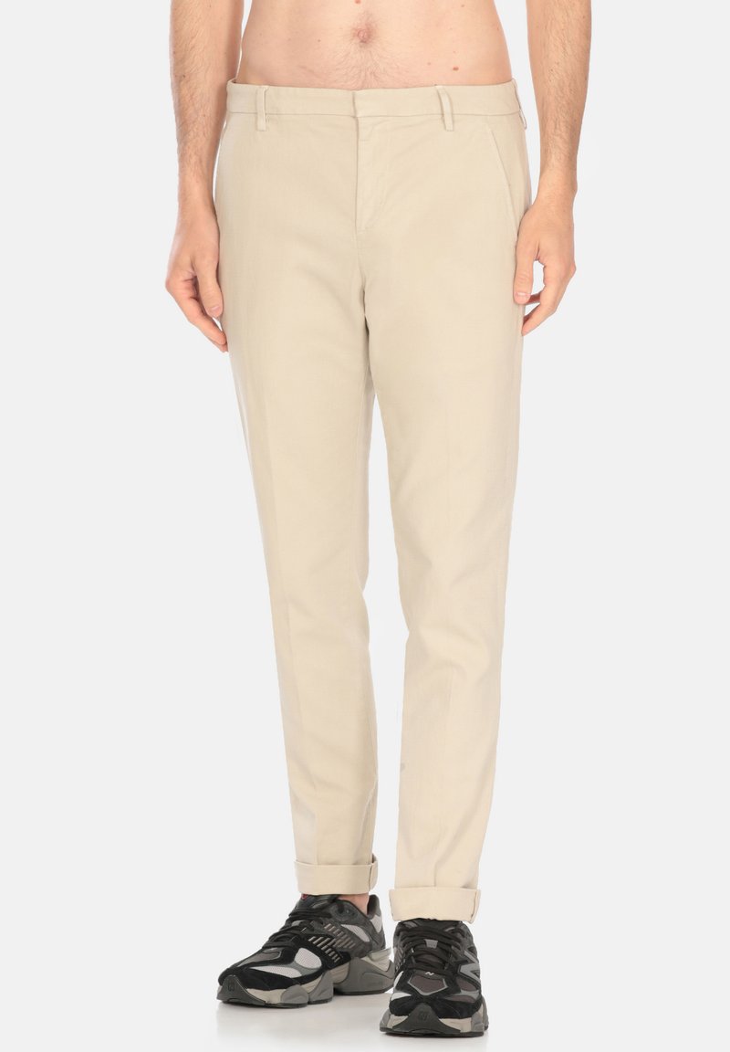 Chino beige con una vestibilità slim, dotati di passanti per cintura e con risvolti, abbinati a sneaker nere. Tessuto liscio e design sartoriale.