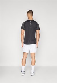 Men's black athletic shirt with mesh-textured sleeves, featuring "ENDLESS" printed vertically on the back, paired with white shorts.