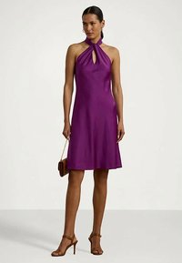 Naine kannab ilma varrukateta lilla rinnahoidja kleiti, millel on võtmeaugu kaelus, hoiab käes pruuni kotti ja jalas on tal pruunid kõrge kanna sandaalid.