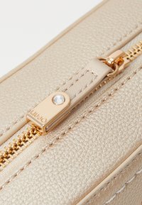 Beige Lederbeutel mit strukturierter Oberfläche, ausgestattet mit einem goldenen Reißverschluss mit Kristallakzent und gestickten Details entlang der Kanten.