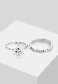 Dva strieborné prstene na bielom povrchu: jeden s veľkým okrúhlym solitérnym kameňom, druhý pásik so zabudovanými menšími kameňmi.