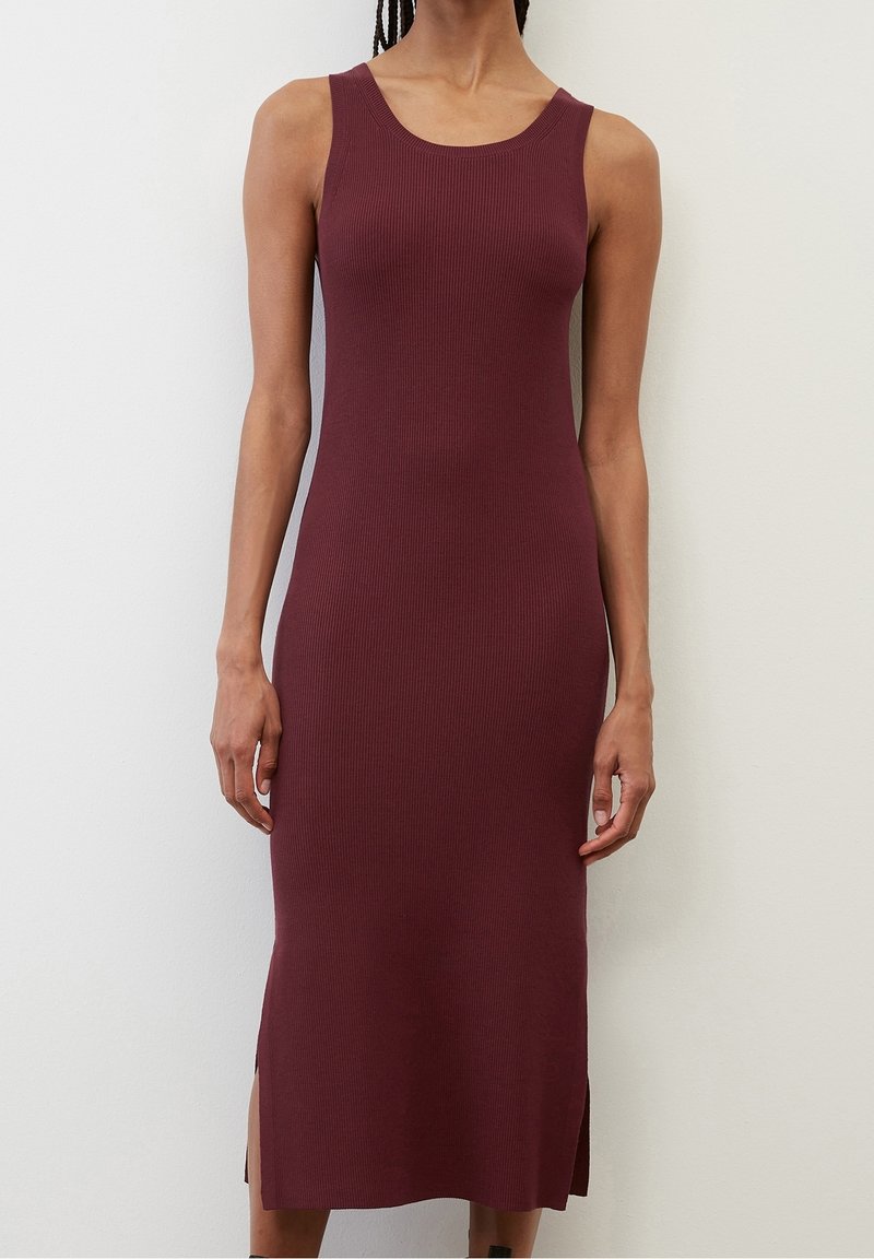 Robe midi bordeaux sans manches, côtelée, avec fentes latérales, portée par une personne debout contre un mur clair uni.