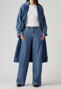 Denim trench coat with long sleeves, paired with wide-leg blue jeans and a white fitted top. Smooth texture, classic blue wash, minimal detailing.