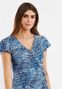 Vestido azul y blanco con un diseño de wrap, mangas cortas y vaporosas, y un detalle de lazo en la cintura, con una tela texturizada.