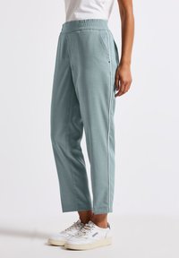 Helleblaue, taillierte Hose mit elastischem Bund und seitlichen Paspeldetails. Aus einem glatten Stoff gefertigt und mit Seitentaschen ausgestattet.