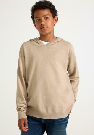 Beige Hoodie mit langen Ärmeln, V-Ausschnitt und Kordelzugkapuze. Weicher Stoff mit gerippten Bündchen und Saum. Kombiniert mit blauen Jeans.