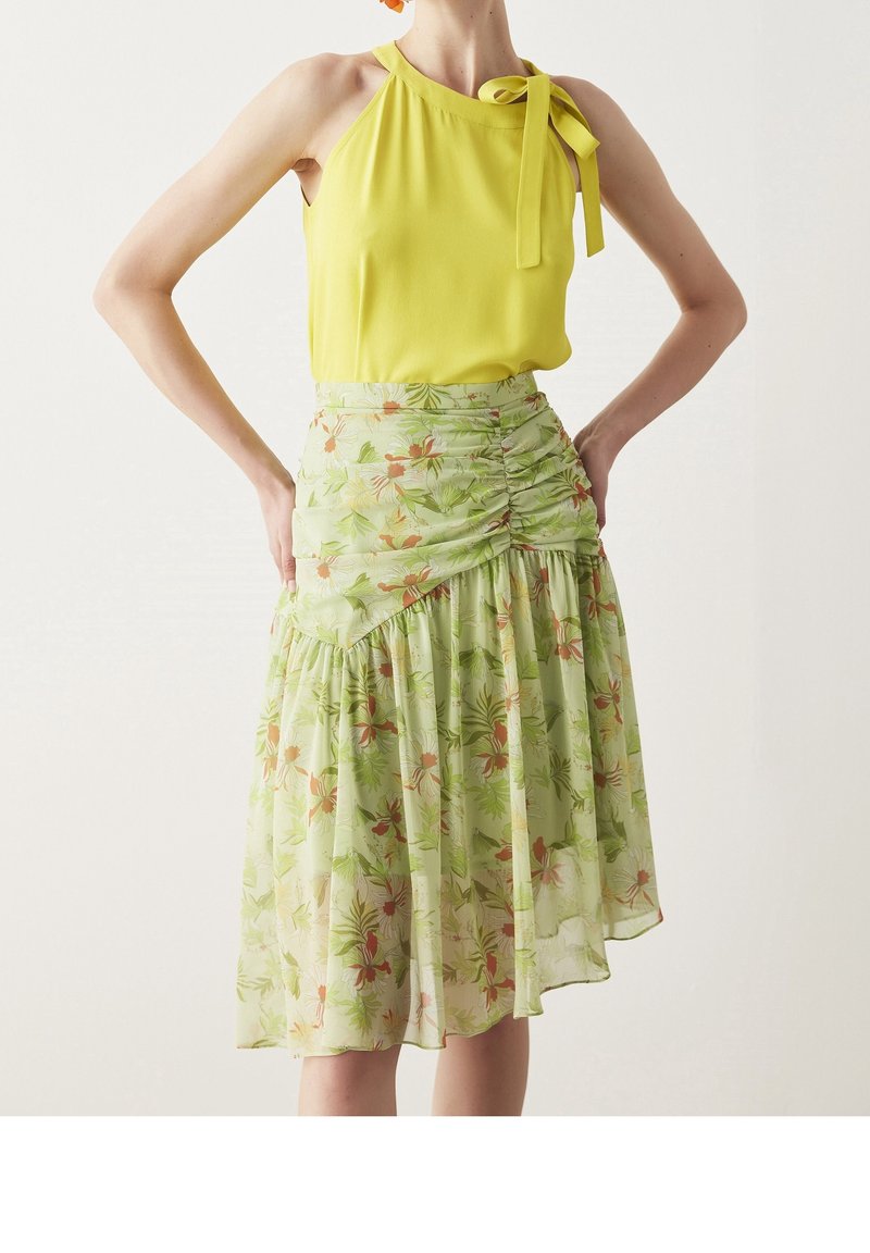 Haut dos nu jaune avec un détail en nœud, associé à une jupe à motifs floraux verts, présentant des fronces et des couches de tissu pour une silhouette fluide.