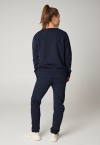 Námořnická modrá mikina a odpovídající tepláky vyrobené z měkké tkaniny. Tento outfit má volný střih, vroubkované manžety a hladkou texturu.