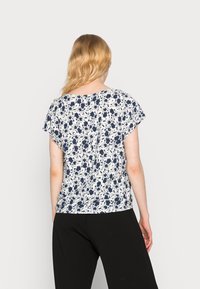 Top floral de manga curta com fundo branco e padrão floral azul, de corte relaxado e decote redondo. Combinado com calças pretas.