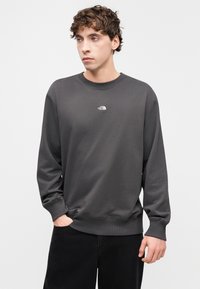 Γκρι φούτερ κατασκευασμένο από λείο ύφασμα, με στρογγυλή λαιμόκοψη και μακριά μανίκια. Μικρό λευκό λογότυπο στο στήθος. Μαύρο παντελόνι.