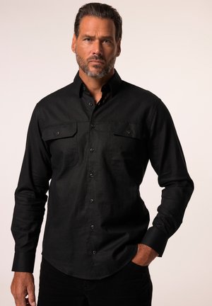 Camisa negra de botones con tejido suave; cuenta con dos bolsillos en el pecho, mangas largas y un dobladillo curvo. Se aprecia una textura sutil.
