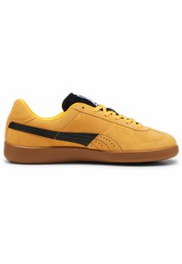 Geel suède sneakers met zwarte accenten, rubberen buitenzool, ronde neus en platte veters. Subtiele perforaties kenmerken het ontwerp aan de zijkant.